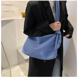 Detail of blue nylon crossbody bag with adjustable strap worn over a black blazer
