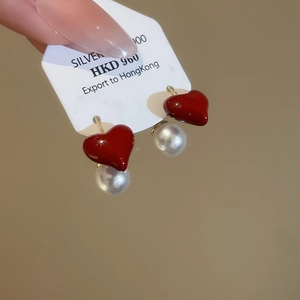 Dettaglio di orecchini a cuore rosso con perle e perni in argento su un cartellino