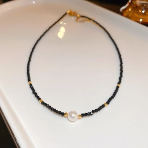 Détail du collier de perles noires facettées avec une perle blanche et accents dorés