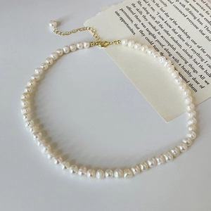 Natural freshwater pearl necklace with gold lobster clasp and extension chain on a white surface