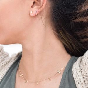 Detail of minimalist gold chain necklace with bar pendants and sparkling stud earrings
