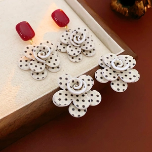 Détail de boucles d'oreilles roses à pois en acrylique avec touches de rouge sur bois