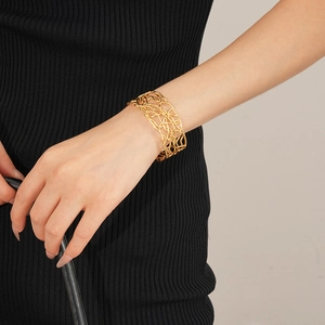 Détail d'un large bracelet manchette plaqué or au design géométrique ajouré sur poignet