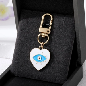 Detail of white enamel heart evil eye pendant with polished gold clip on black velvet