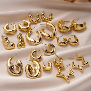 Detailed display of assorted gold geometric stud earrings on soft beige silk fabric