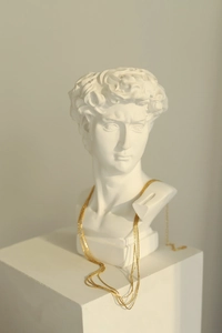 Artistic display of layered gold snake bone necklaces draped over a white Greek plaster bust