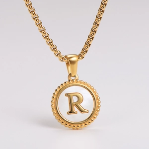 Macro view of gold-plated necklace featuring a white shell pendant with a 3D R letter