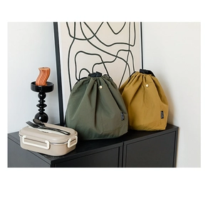Detail of waterproof drawstring lunch bags in dark green and yellow with snap pocket
