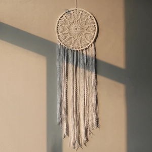 Detailed view of handmade white lace dreamcatcher with long tassels on a sunlit wall