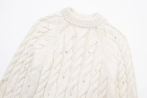 Detailansicht eines weißen Strickpullovers mit Zopfmuster und funkelnden Strassverzierungen
