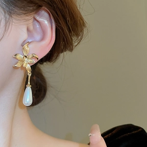 Close-up of elegant gold flower earrings with drop pearls worn on a model's ear