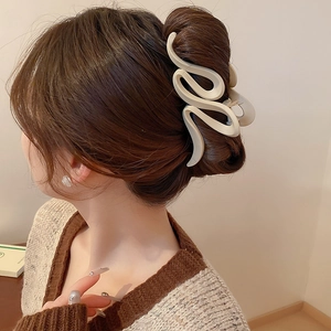 Detail view of large beige matte claw clip with S-curve design on styled hair
