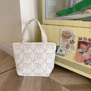 Close-up of white quilted tote bag featuring detailed dark rabbit embroidery and soft texture