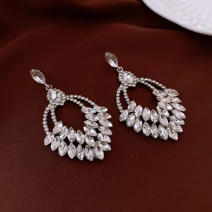 Detailed macro of rhinestone wheat tassel earrings on deep red satin fabric background
