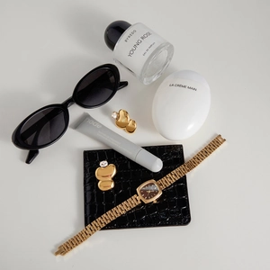 Flat lay of gold oval zircon earrings with a black leather wallet and accessories