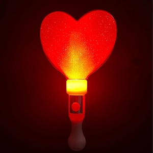 Close-up of glowing heart-shaped LED wand with red glitter texture in a dark background