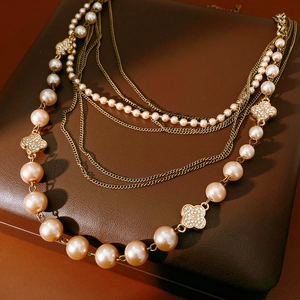 Macro shot of multi-layer pearl necklace featuring diamond-paved clover motifs on leather