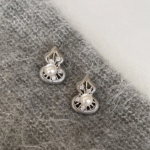 Macro detail of silver gourd earrings with white pearl and zircon on soft fabric