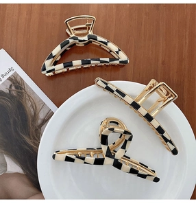 Three geometric checkered hair clips with black and white patterns on gold metal frames