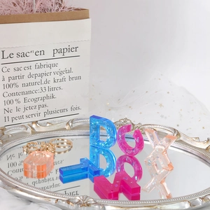 Macro detail of DIY resin alphabet keychains with glitter and gold foil on a mirror tray