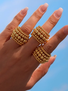 Macro shot of gold layered beads rings on finger with blue sky background