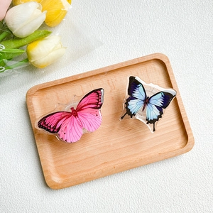 Detail of pink and blue acrylic butterfly phone socket grips on a wooden tray