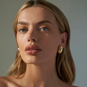 Polished 18k gold plated stainless steel oval bean stud earrings worn by a model