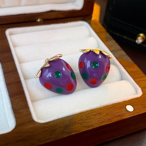 Detailed view of purple strawberry earrings with golden leaves in a luxury wood jewelry box