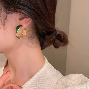 Close-up of a model wearing the green enamel C-shaped metal earring with gold finish