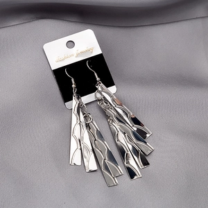 Detail of layered silver tassel earrings with geometric wave textures on metal strips