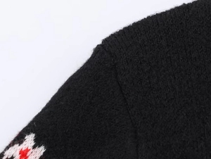 Detail van schoudernaad met rood en wit geometrisch jacquardpatroon op zwart gebreid