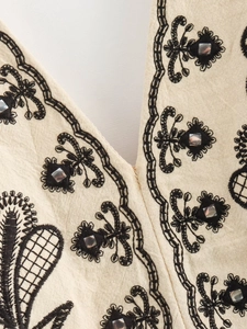Detail of beige cotton linen fabric with black embroidery and square sequins