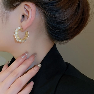 Detailed view of a gold-wrapped crystal C-shape earring worn on a model's ear