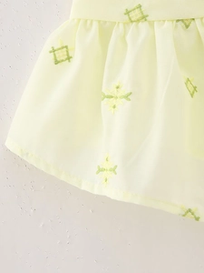 Vue macro du tissu jaune clair avec broderie géométrique verte et détails volantés