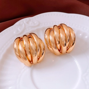 Détail de boucles d'oreilles dorées avec textures multicouches et finitions polies