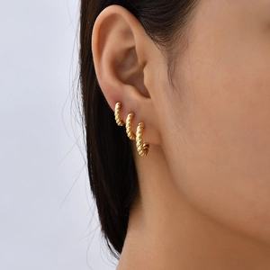 Close-up of a model wearing three layered golden twisted rope cuff earrings