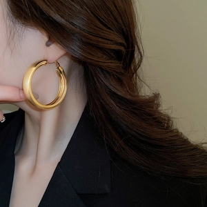 Close-up of model wearing large matte gold hoop earrings with a thick brushed metal finish