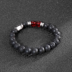 Detail of volcanic stone bracelet with red beads and silver charms on black texture