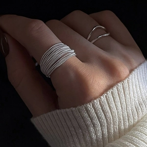 Anillos minimalistas de plata multicapa en la mano con suéter de punto blanco
