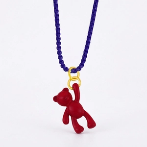 Close-up of a cute red bear pendant with golden rings and a dark blue braided chain