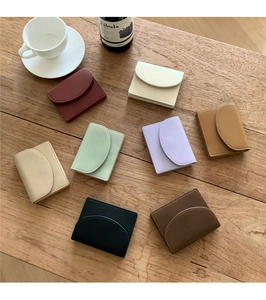 Flat lay of minimalist leather card wallets in eight assorted colors on a wood surface