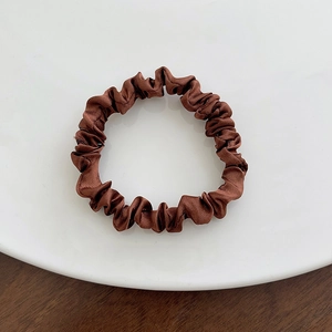 Brown satin scrunchie with pleated texture on a white plate over a wooden background