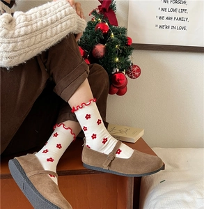 Detail of white cotton socks with red floral print and ruffled cuffs worn with brown shoes