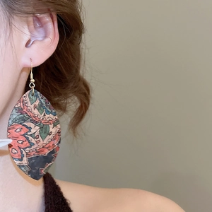 Detailed view of bohemian leaf-shaped leather earrings with vintage ethnic print worn by model