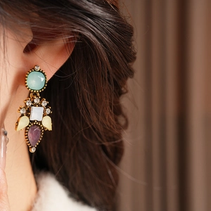 Close-up of vintage gold earrings featuring colorful faceted gemstones on model