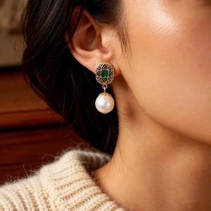 Side view of model wearing vintage gold earrings with green gems and white pearls
