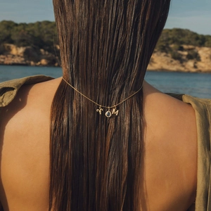 Détail de pendentifs Bélier doré et lettre M avec pierre précieuse bleue dans les cheveux