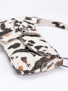 Detailed close-up of cow print shoulder bag with silver studs and metal buckle closure