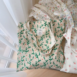 Detailed macro view of the floral canvas tote bag featuring dense green leaves and red flowers