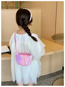 Pink sequin crossbody bag with angel wings shown on a young girl in a bright room